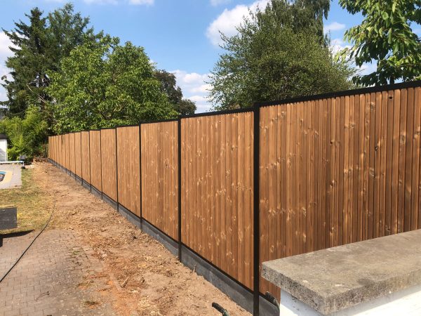 Verticale tand en groef thermo vuren planken met aluminium palen, antraciet betonplaat en zowel boven- als onderaan voorzien van afdekprofiel